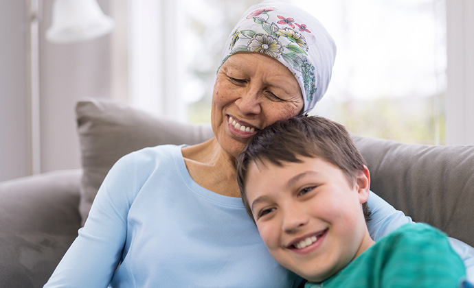 A woman wearing a head scarf hugs a boy as they sit on a sofa