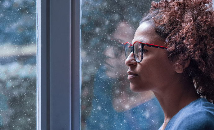 A woman looks out a window at the rain