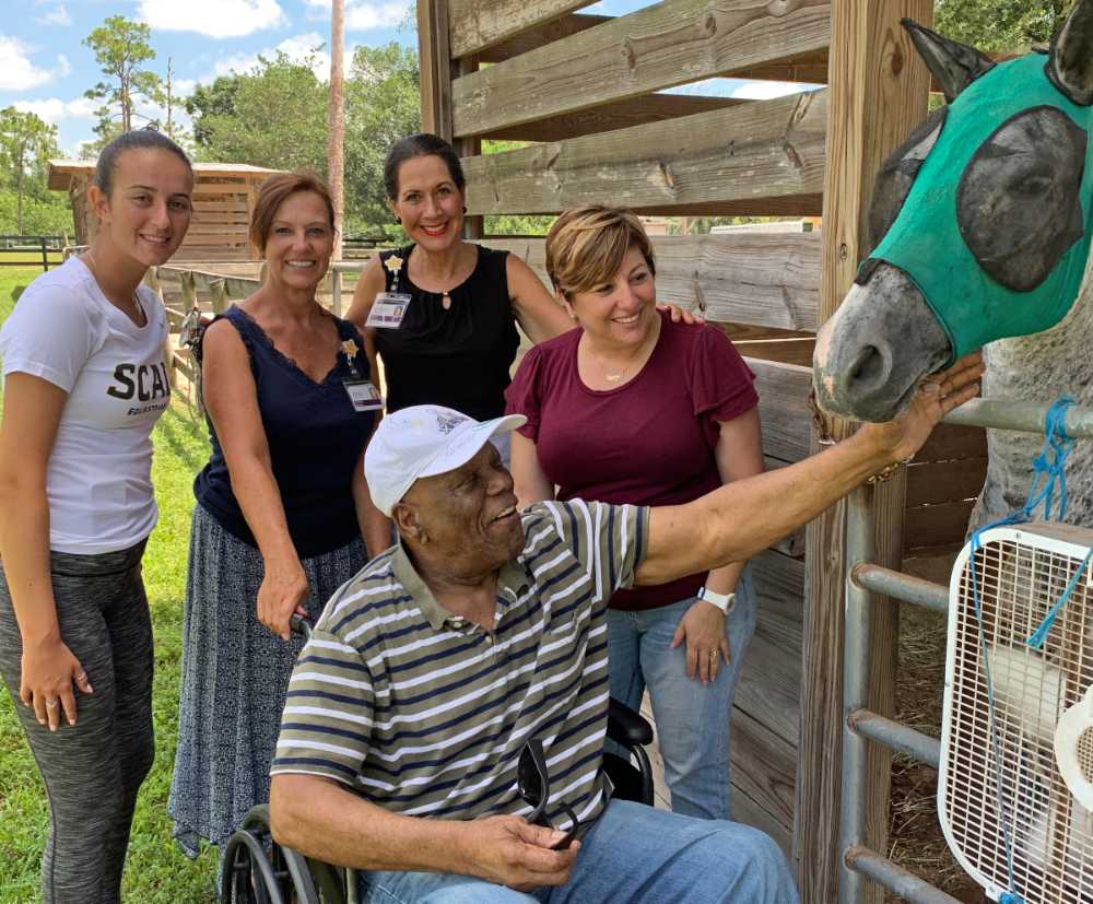 The team stands behind Roy as he touches Colin, a gray male horse, at a stable