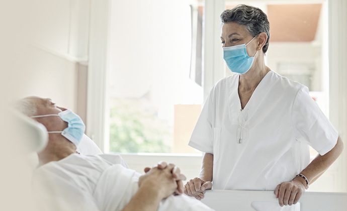 A clinician talks with a male patient who is lying in bed