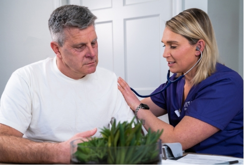 A nurse holds a stethoscope to a man's chest