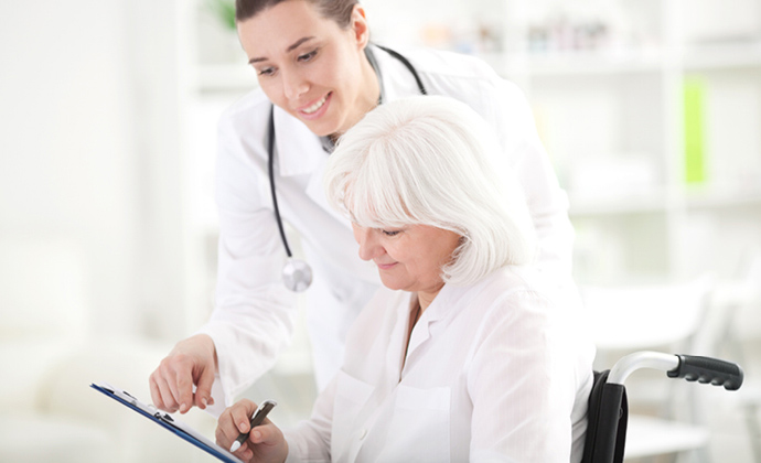 A physician reviews a document with a woman who is seated in a wheelchair